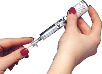 A pair of hands with red painted finger nails use the syringe magnifier to fill their syringe with the proper amount of medicine.