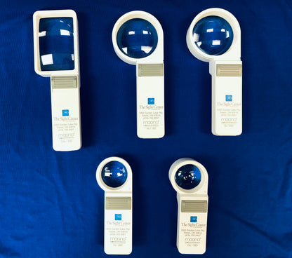 5 Magno Hand Held Magnifiers are on display. The magnifiers are 3.5x, 4x, 5x, 7x, and 10x. The 3.5x is rectangular and the rest are round. They vary in sizes. The magnifiers and white with a gray on/off switch. The Sight Center's logo and contact information is printed on the magnifier.