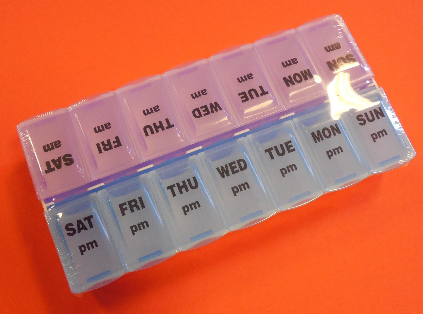A pill organizer that is split down the middle. One side has Sunday through Saturday AM in pink. The other side has Sunday through Saturday PM in blue.