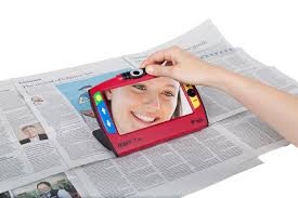 A person's hand holding a Ruby 7 HD over a picture in a newspaper