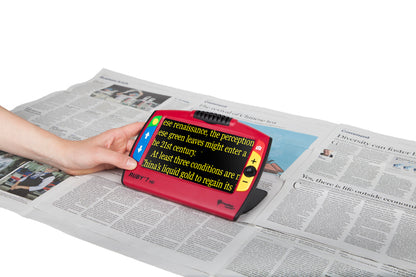 A person's hand holding a Ruby 7 HD over a newspaper article